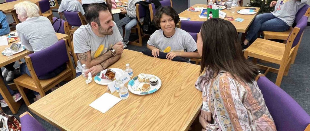 a smiling man looking at a young smiling boy who is talking to another adult