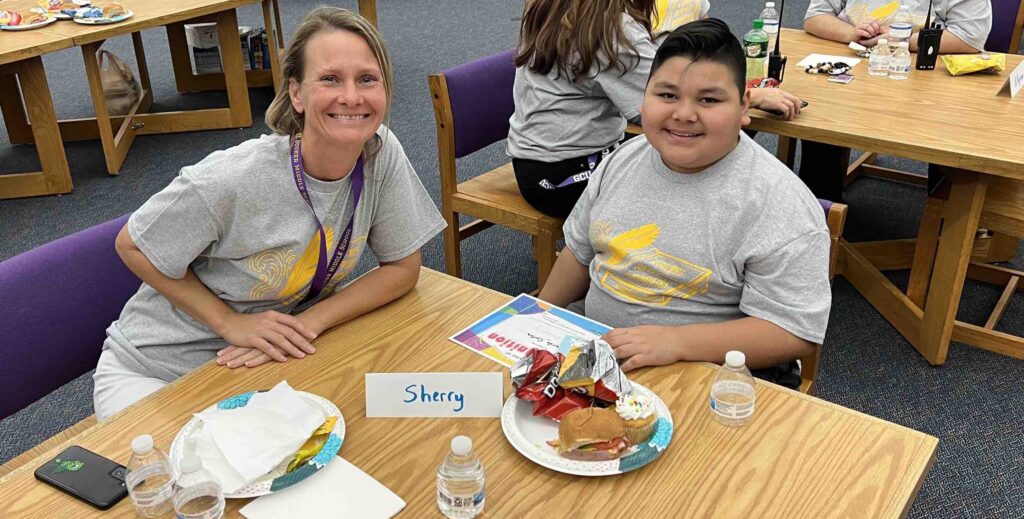 A smiling blond woman sitting at a table with a middle school boy