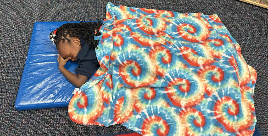 child sleeping on a blue mat with a rainbow blanket